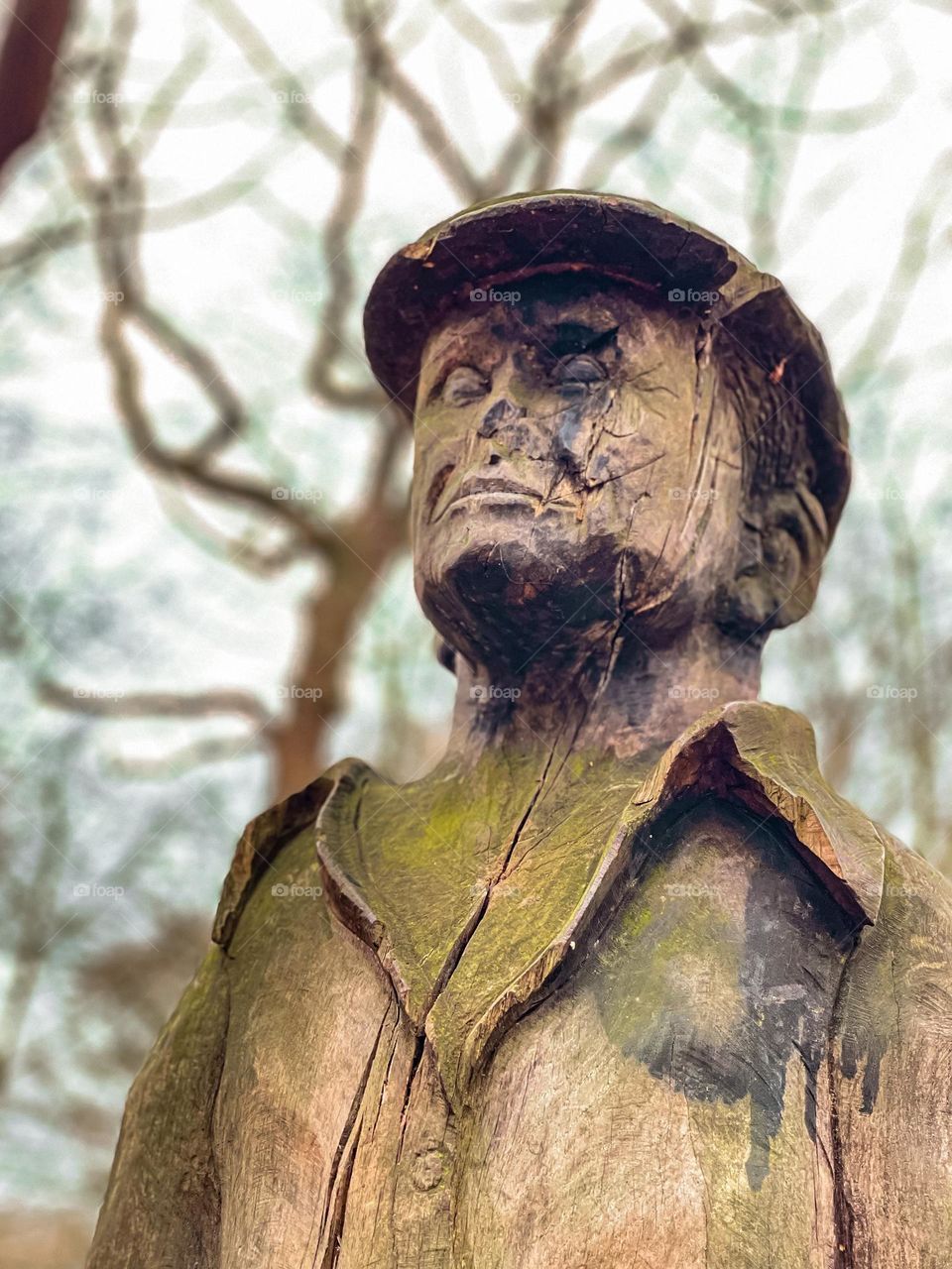 Wooden man carving aged in moss trees in background