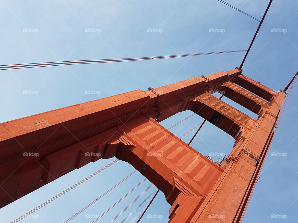 view looking up to red colored Golden Gate Bridge in San Francisco, America, on sunny blue sky day