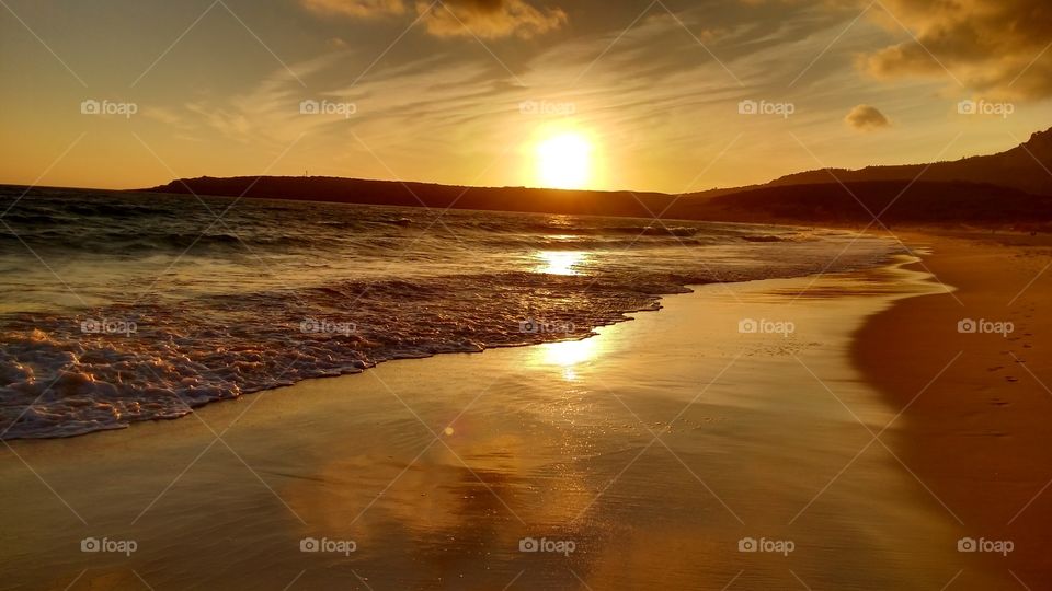 Atardecer en la playa de Bolonia sobre su famosa duna, con reflejos en el agua de las nubes en la orilla de la playa