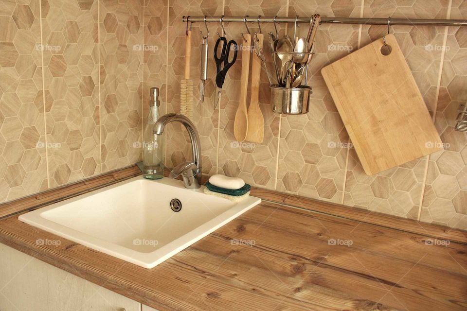 White sink with wooden and steel kitchen utensils in the kitchen in eco scandy style