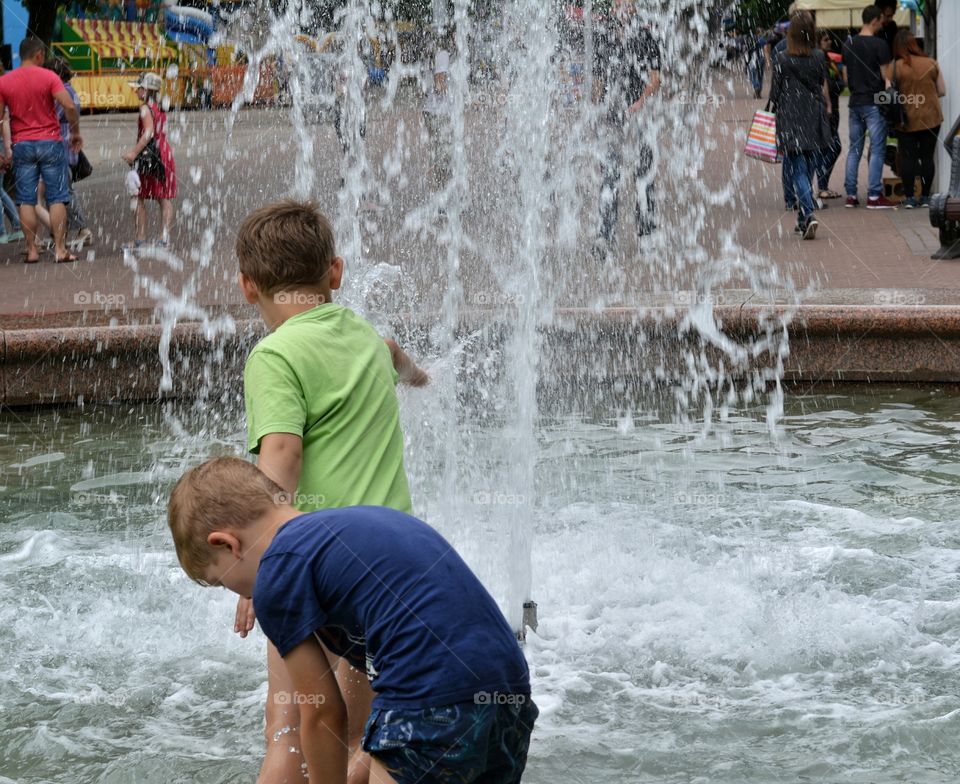 children boys in the water splash fountain, summer heat, city street view