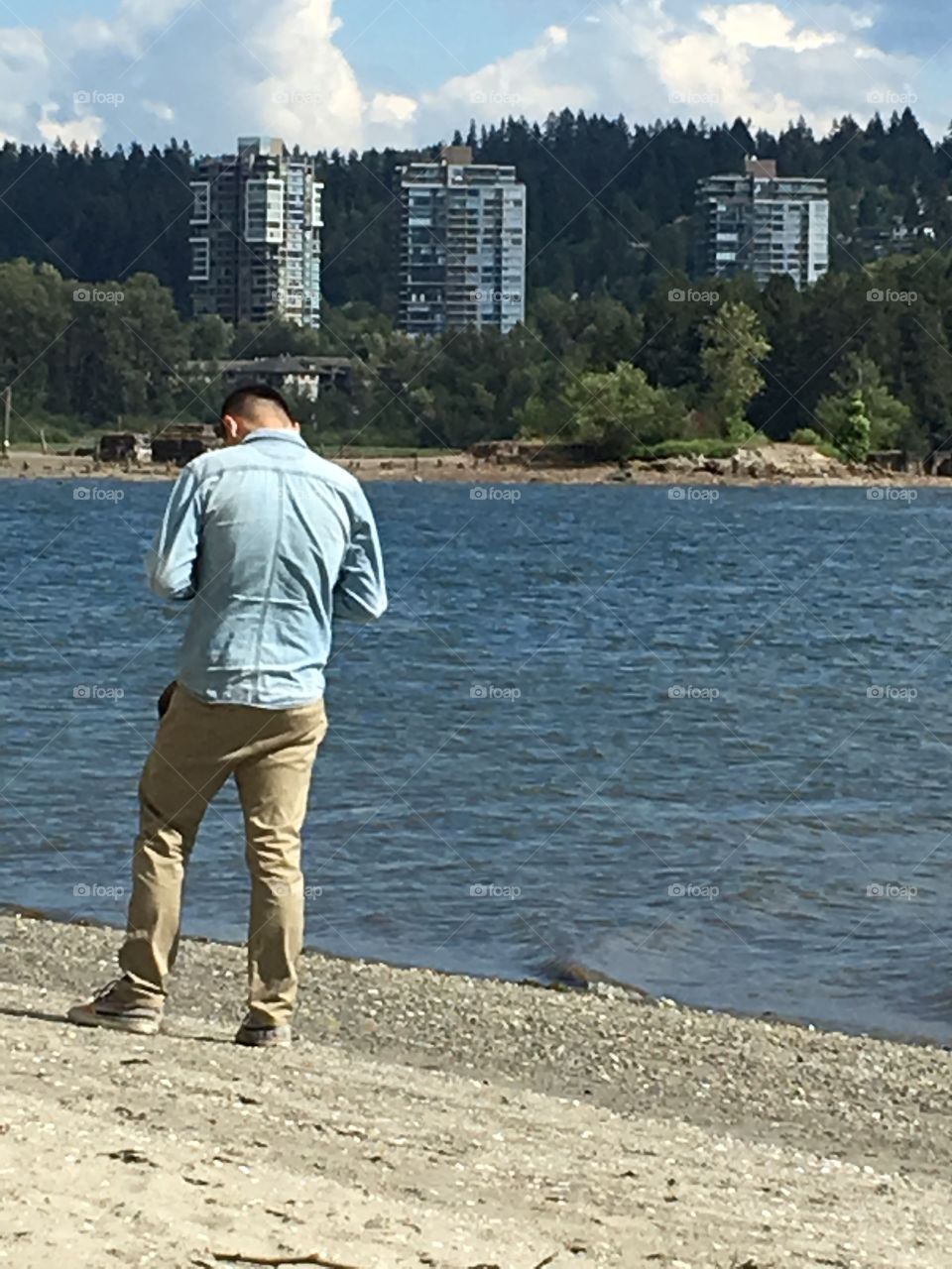 Young Asian male on beach stopping to use cellphone 