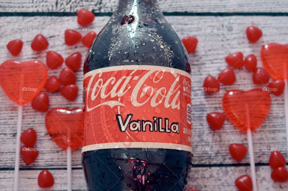 A plastic bottle of Coca-Cola vanilla with candy hearts and a white rustic