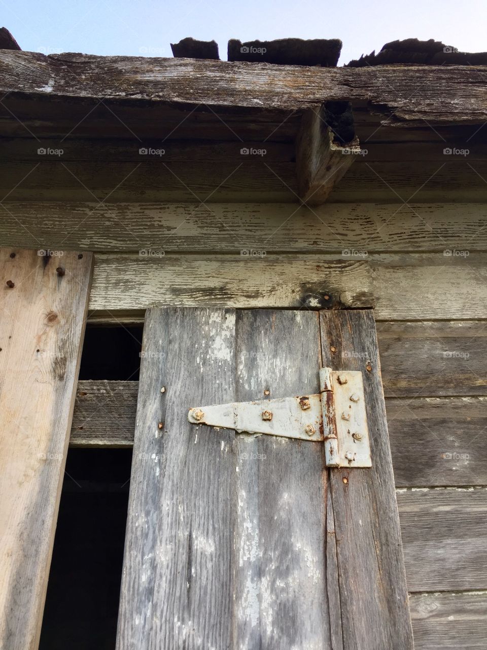 View from below the overhang of an antique weathered,farm shed and door to grain storage with rusted hinges with peeling paint