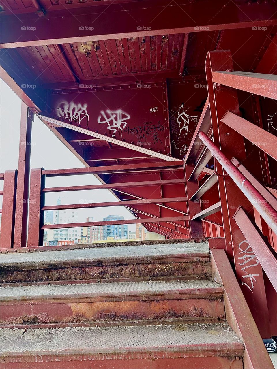 This is the red metal staircase that leads up to the pedestrian lane of the “Pulaski Bridge” at “Newtown Creek” that connects LIC, Queens to “Greenpoint”, Brooklyn. 2024. Hypnotic Productions