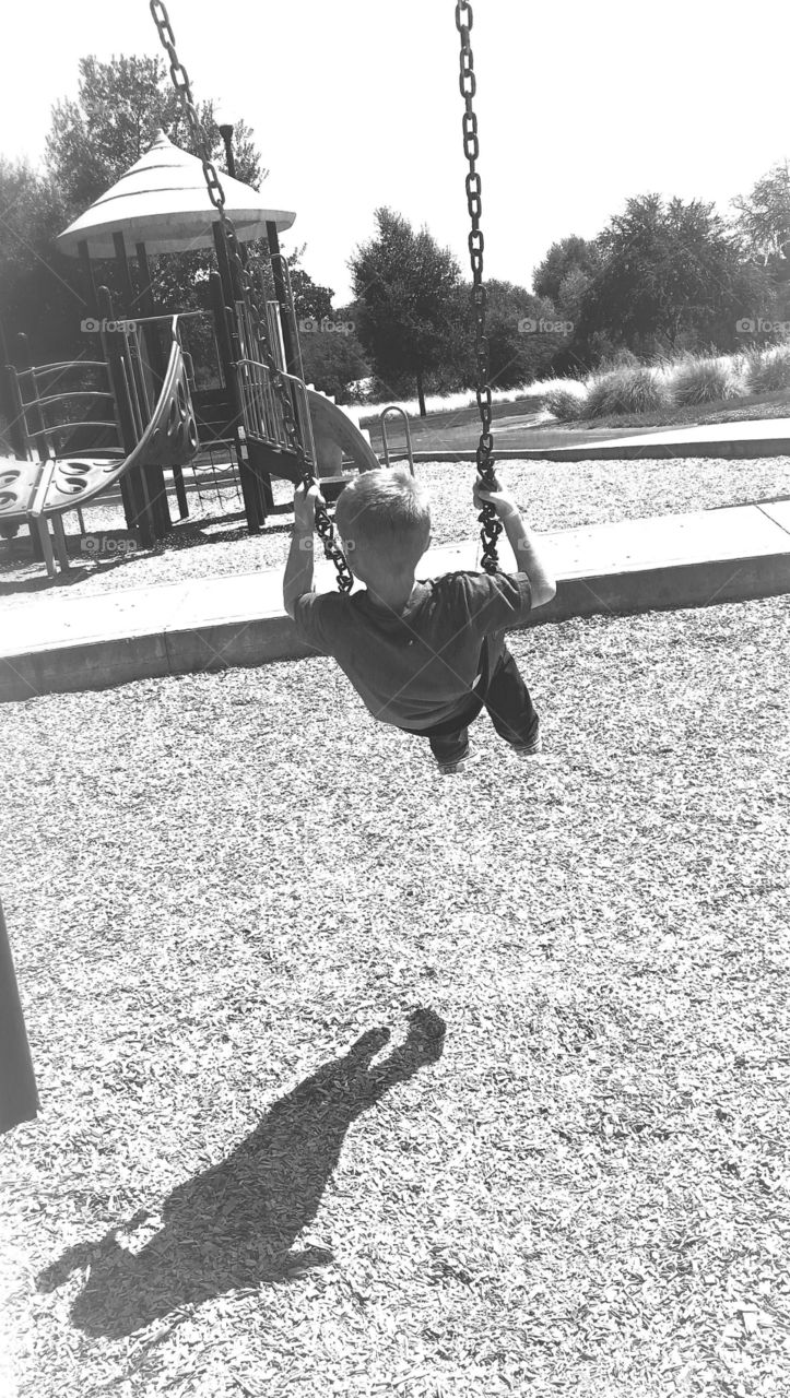 Little boy and his shadow swinging at the park and 