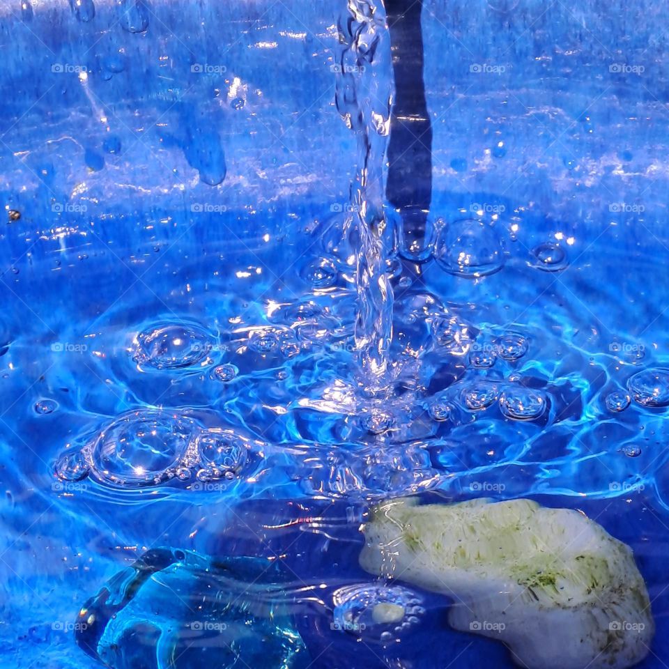blue pot with flowing water cascading into it with shadow in sunlight. droplets
