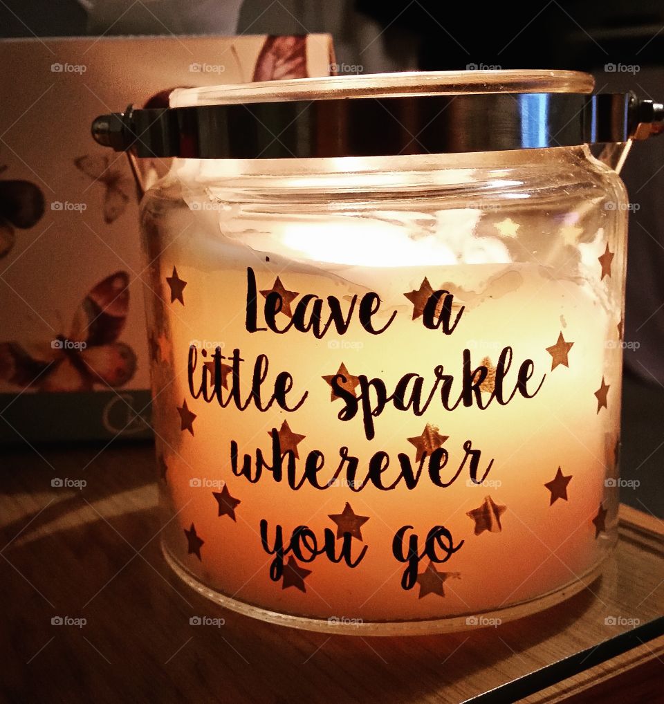 A lit candle in a glass jar with an inspirational quote on the front.