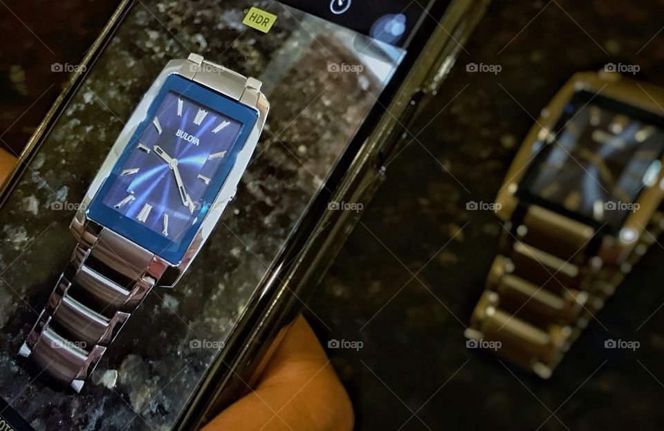 Hand holding a cellphone taking a photo of a watch 