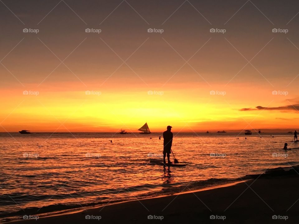Person paddleboarding in sea at sunset