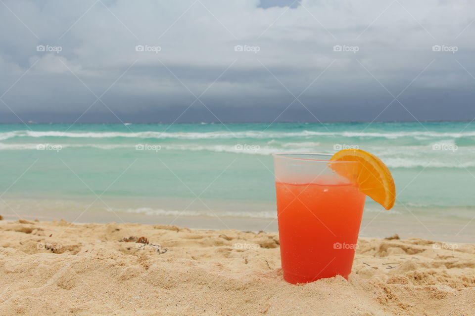 Orange juice glass on sandy beach