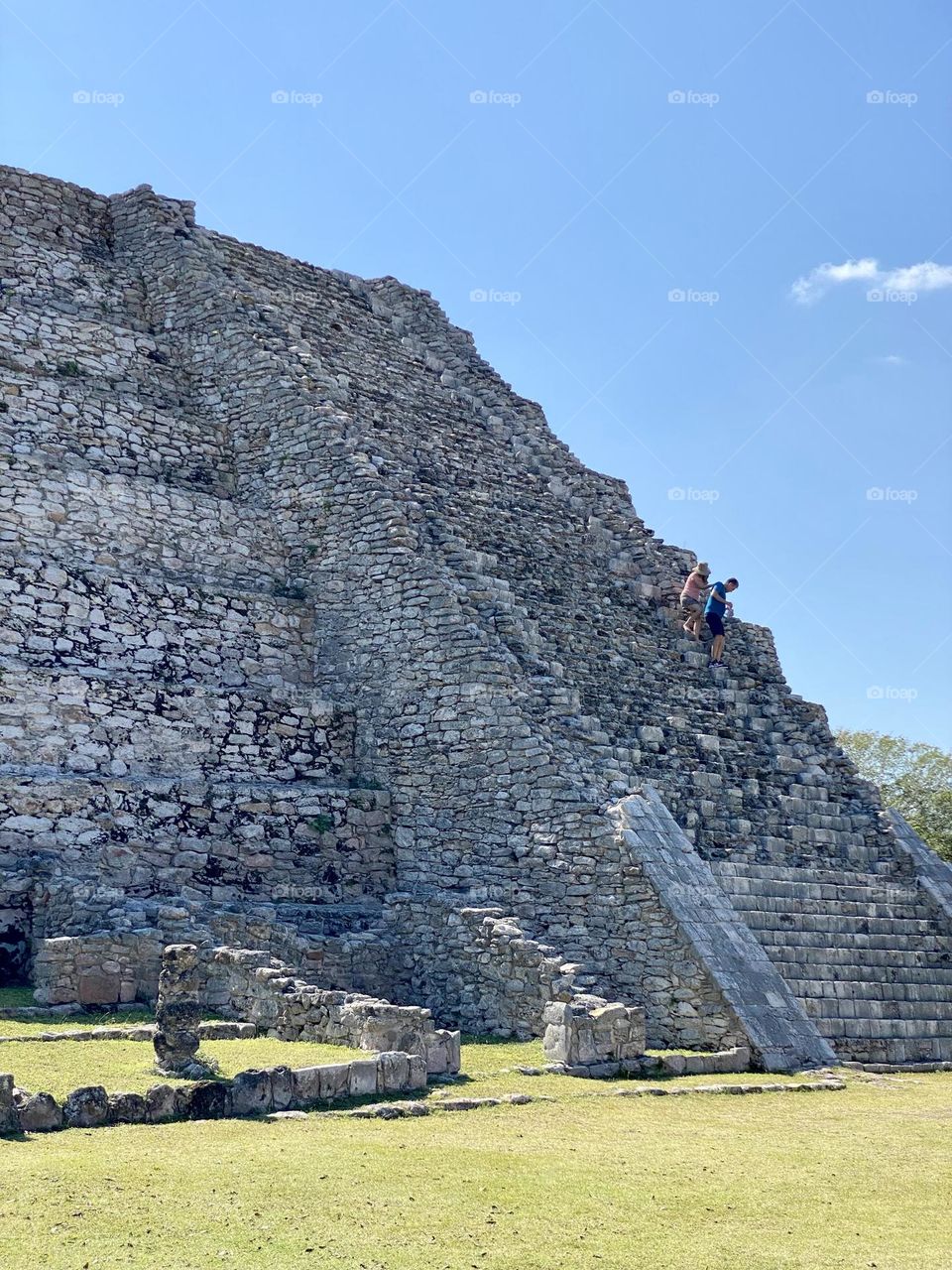 Two people walking down the stairs of an old Mayan temple in Mayapan Mexico 