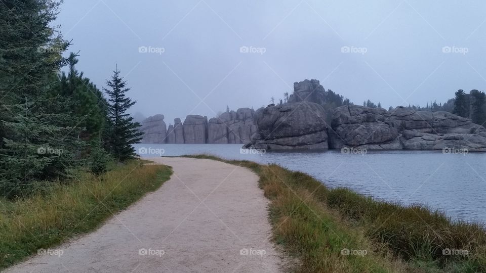 Evergreen fir tree rimmed path along Sylvan Lake with a view of the rocky bluffs