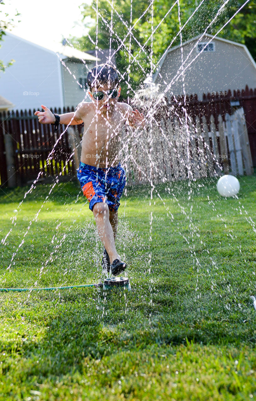 Boy running through a sprinkler in the summer