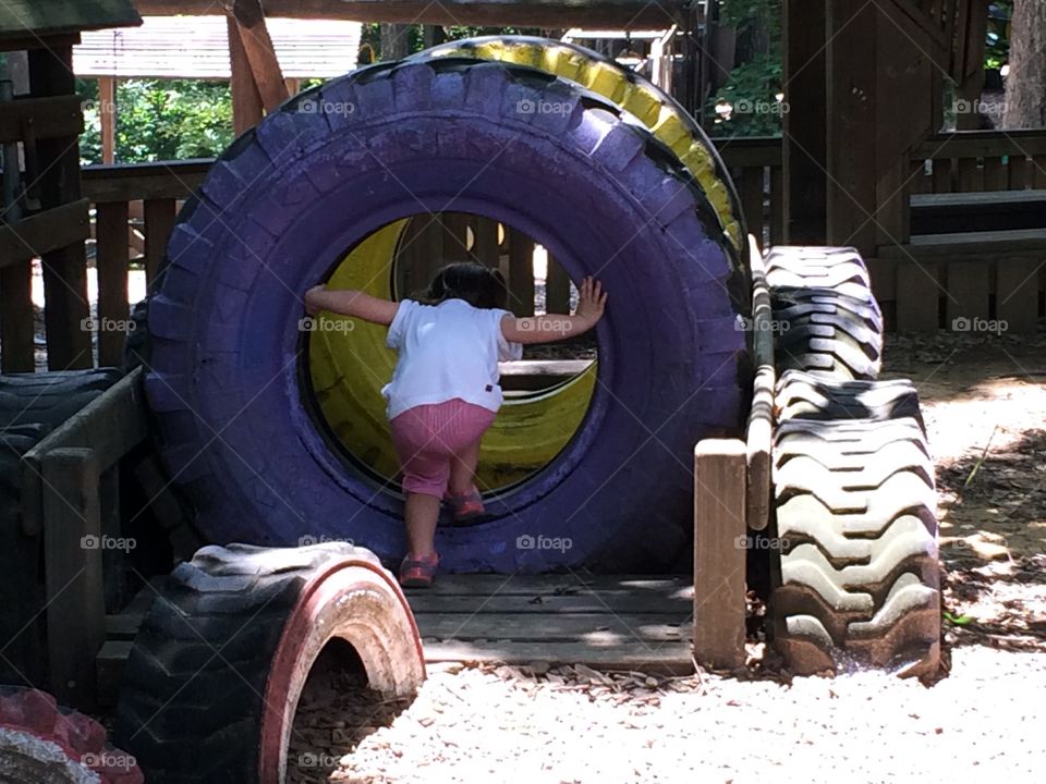 Toddler girl climbing through tire and Exploring the playground playing pretend