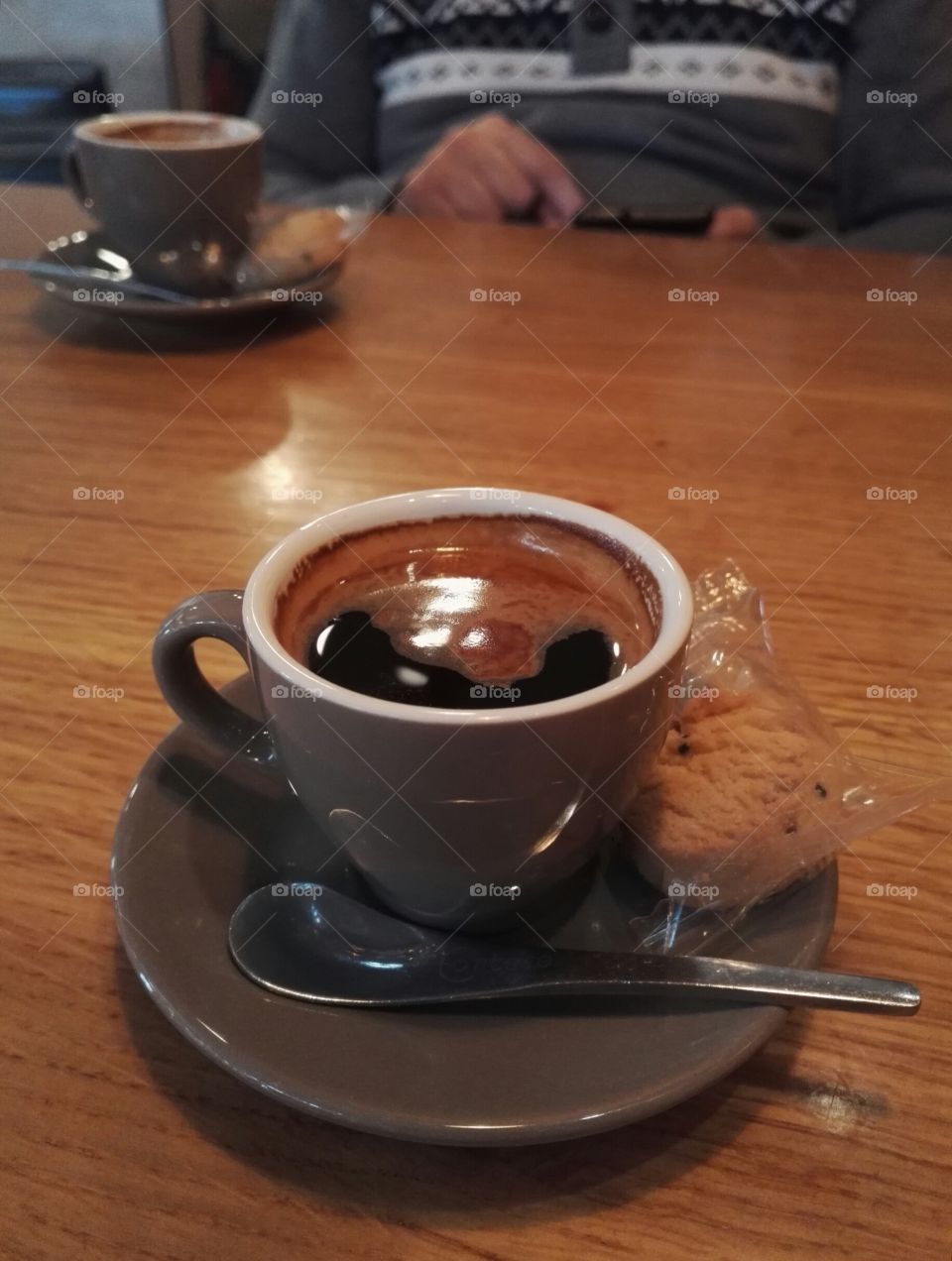 two espresso cups with spoon and cookie and a man with smarphone in the background