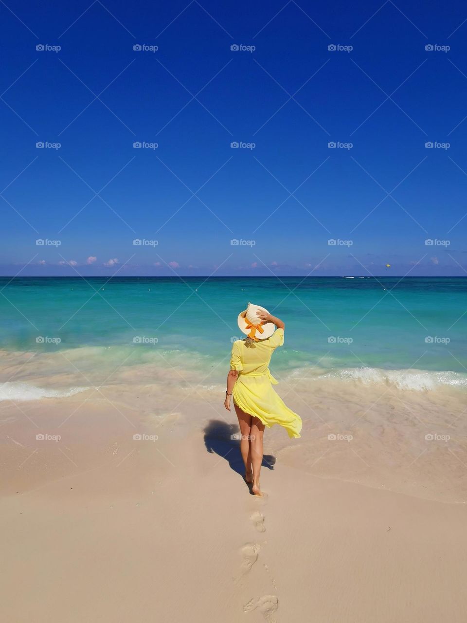 Amazing holiday time in the Dominican Republic. Bavaro beach. Woman in yellow dress an nice hat looks at the sea. Travel photo. Summer time. Sunny weather. Blue sky, blue sea, sun, sand and woman. Time to relax and enjoy sunshine.