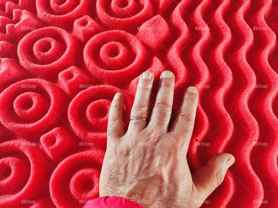 male hand sinks on the red mattress with raised circular designs