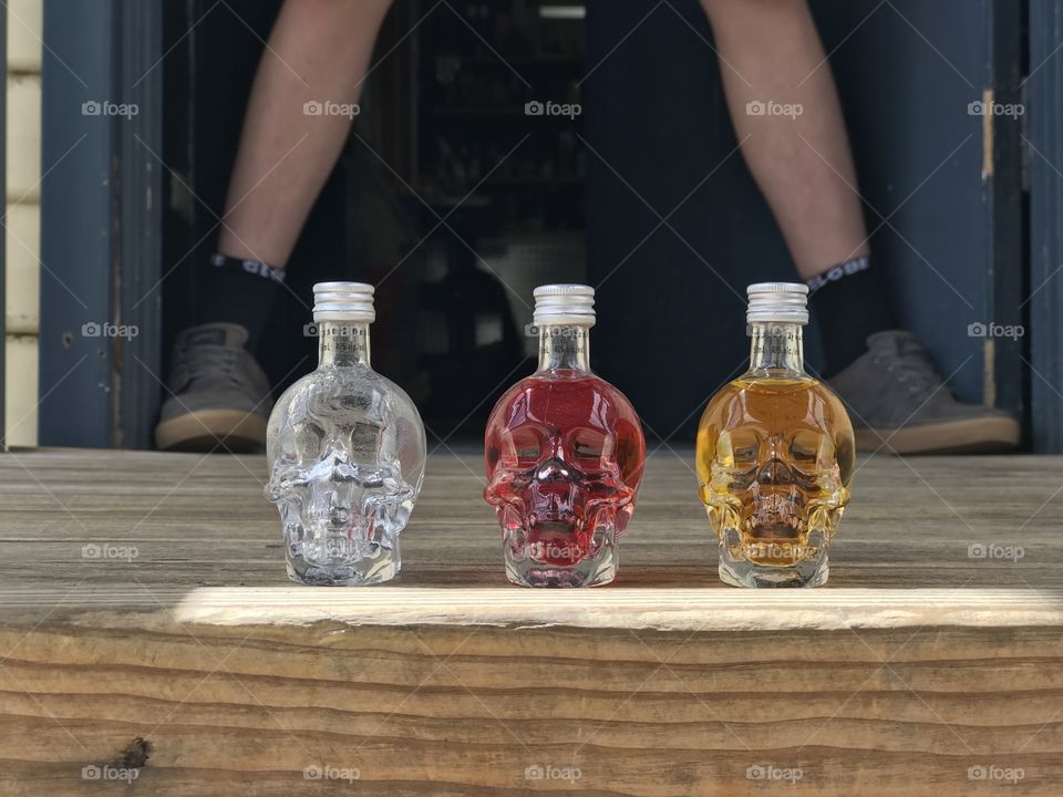 Three small skull bottles of a drink lined up closely. Positioned in the middle of someone’s spread legs in the background making for a nicely positioned image. 