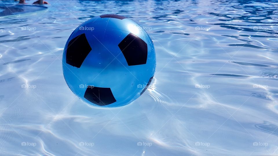 Blue funny plastic football floating on clear water in a swimming pool on a sunny day - bad med en blå boll som flyter på vattnet i en pool med klart vatten en solig fin dag