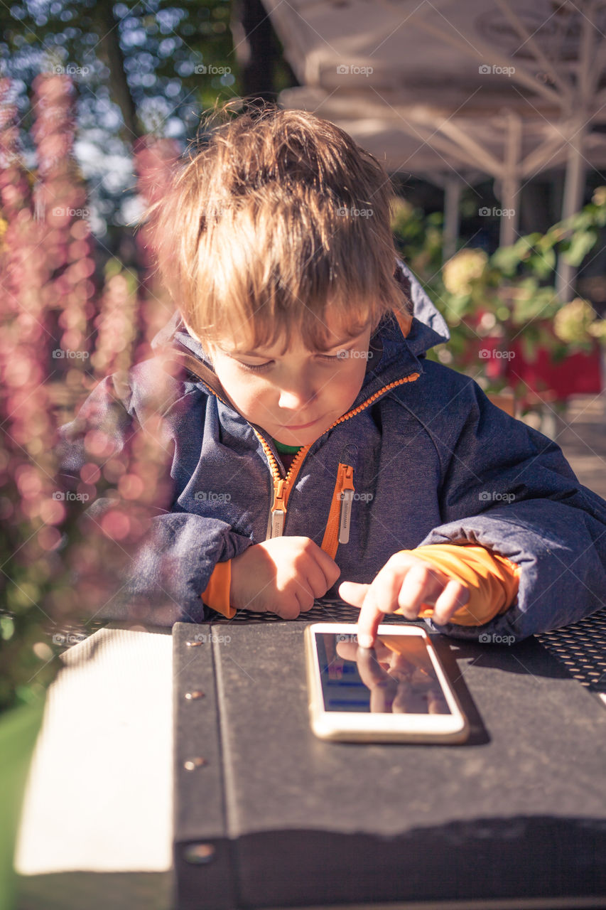 Boy with smart phone on table. Boy looking on a large smart phone, outdoors at table
