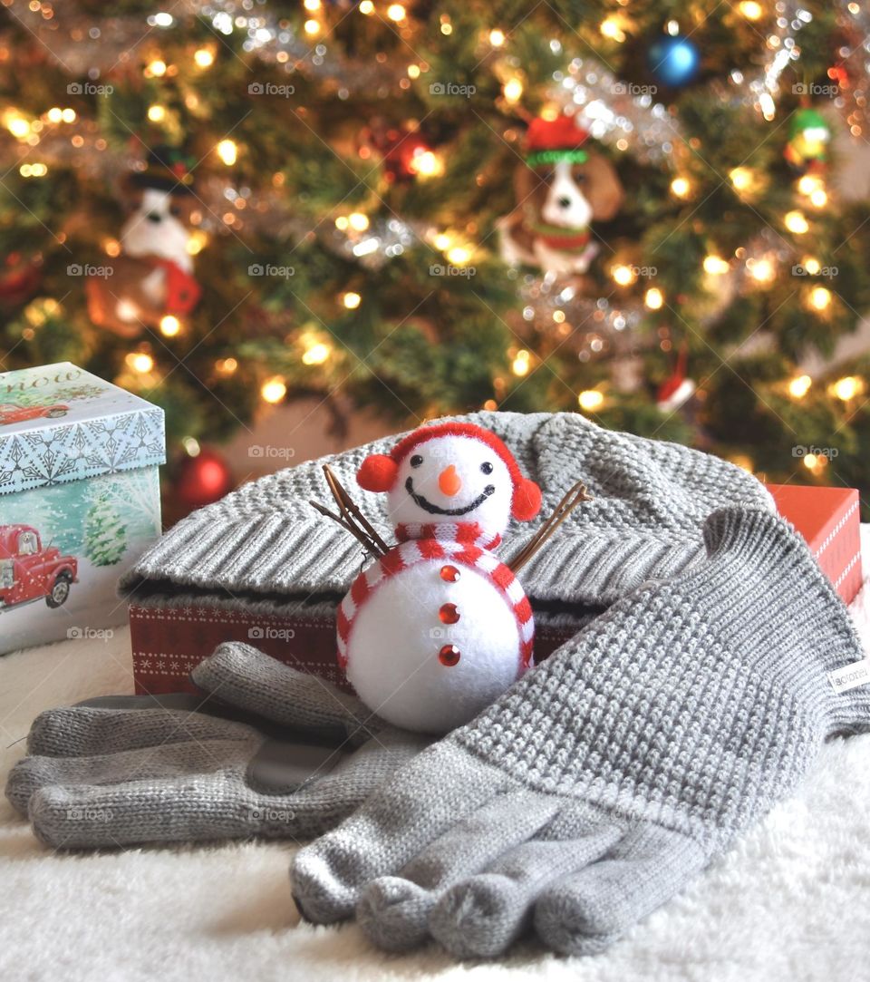 Holidays, Christmas tree in background with gift of gloves and hat in foreground 