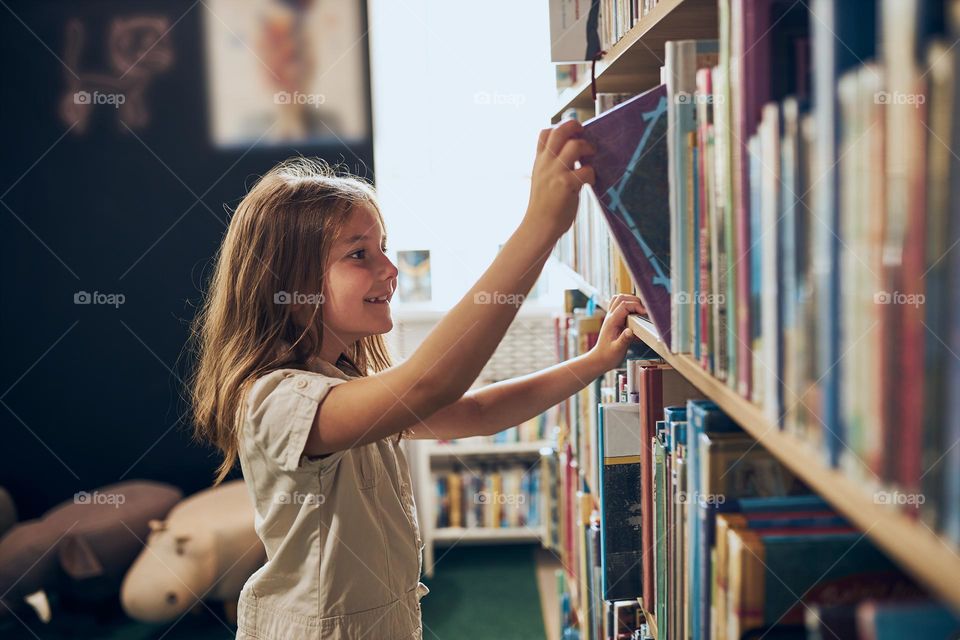 Schoolgirl choosing book in school library. Smart girl selecting literature for reading. Books on shelves in bookstore. Learning from books. School education. Benefits of everyday reading. Child curiosity. Back to school