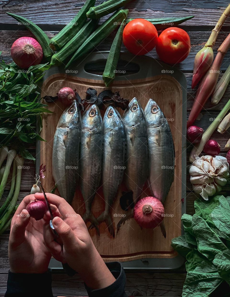 Hands are peeling onions preparing to cook in the kitchen. fresh fish and vegetables on the table.