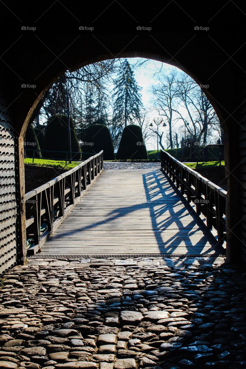 View of the wooden bridge and park through the old gate. Dominance geometric shapes: triangle,  rectangle,  and semicircle