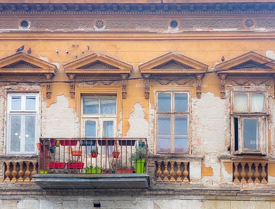 An old building with four windows and a terrace.  Dominance of geometric shapes: rectangle,  triangle, and circles