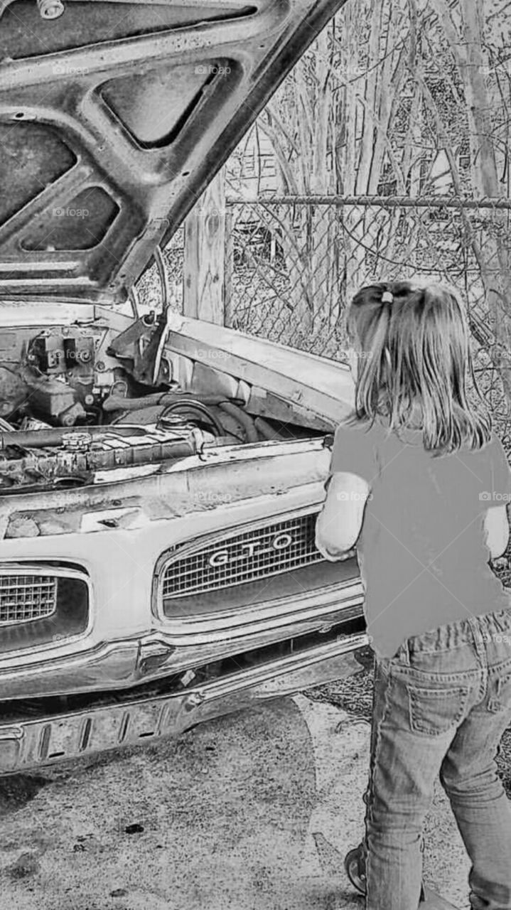 Young girl on scooter looking at gto car with hood up