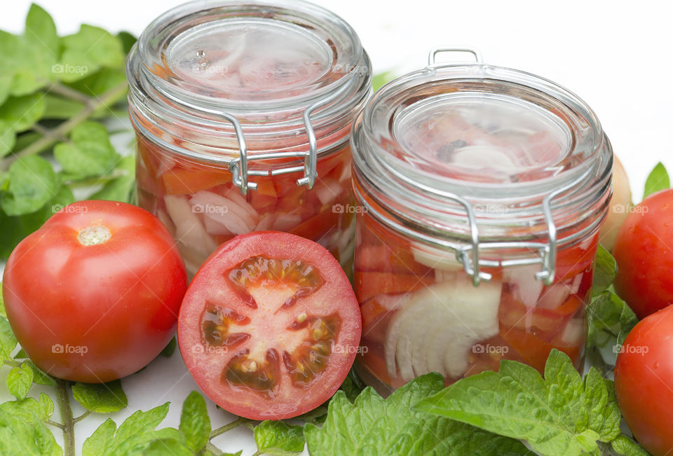 Two glass jars filled with ripe red sliced  tomatoes and chopped onions with tomato halves.