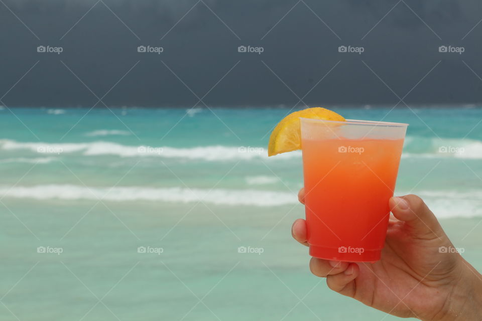 Close-up of hand holding juice at beach