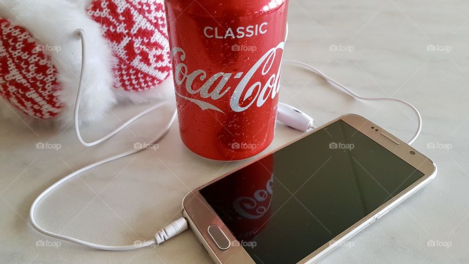 Enjoying a cold Coke while listening to music in my mobile phone by using red and white headphones 
