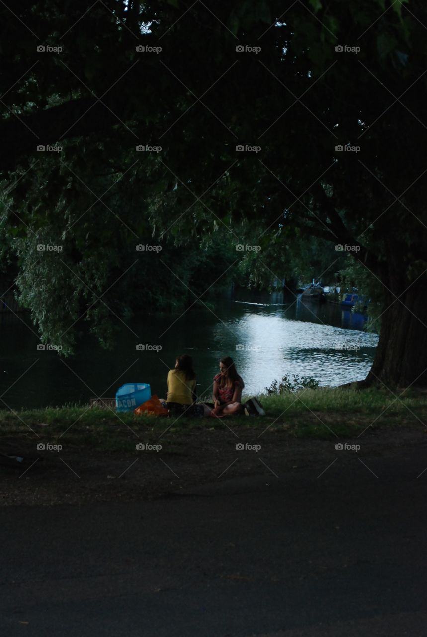 two female friends picnicking by the river in a late afternoon in a warm summer evening