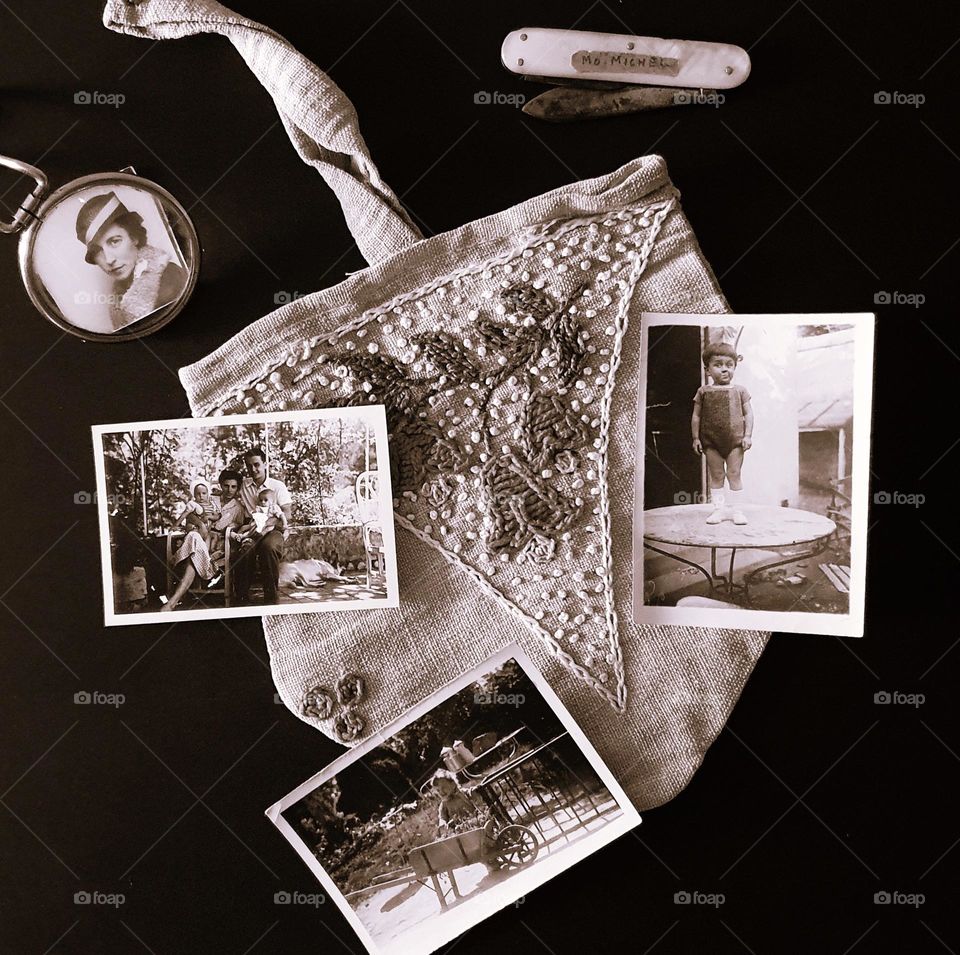 Sepia shot of a vintage flatlay placed on a dark surface composed of a handmade handbag, a mother-of-pearl penknife, a pocket magnifying glass and four old photos
