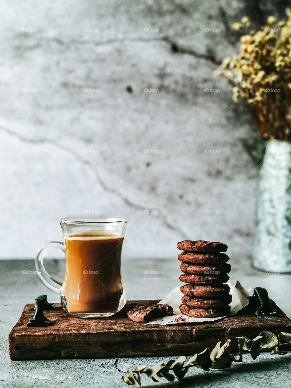 A cup of milk coffee and stack of biscuits on wooden board