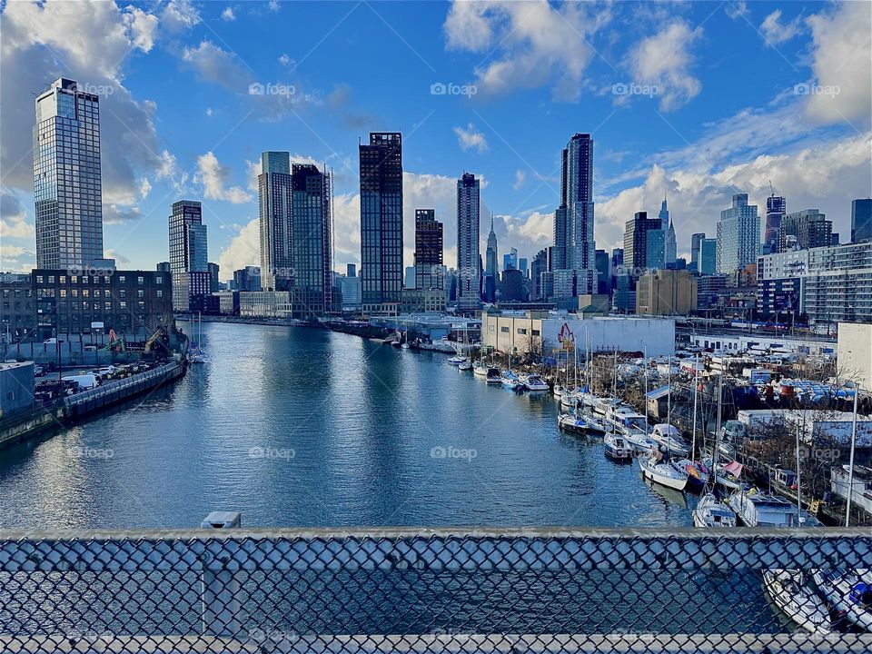 This is “Newtown Creek” seen from the “Pulaski Bridge” that connects LIC, Queens and “Greenpoint”, Bklyn with all its various boats. In the distance we see “Manhattan” incl. the “Empire State Bldg” and the “Kreisler Bldg”. 2023. Hypnotic Productions