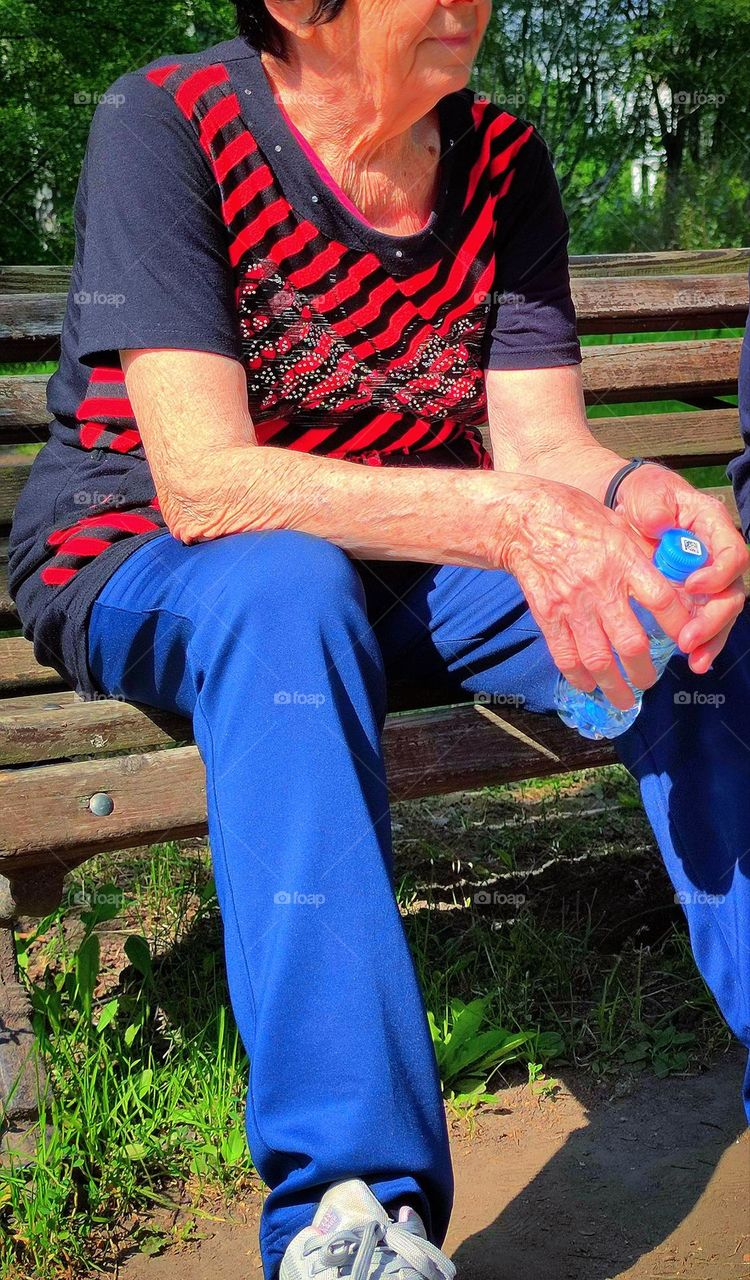 Skin of the face and hands of an elderly woman who is sitting on a bench with a bottle of water