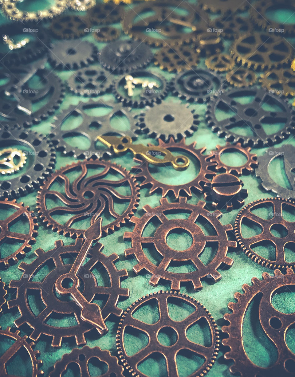 Metal cogs and gears of assorted metals are laid out on a green surface