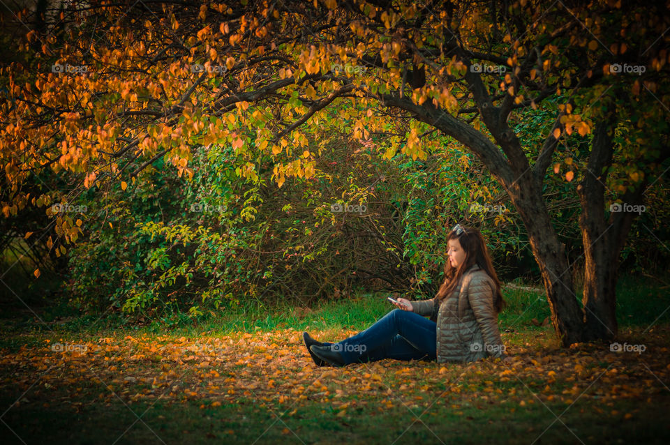 warm autumn day girl sits in a clearing strewn with leaves and holds a phone in her hands