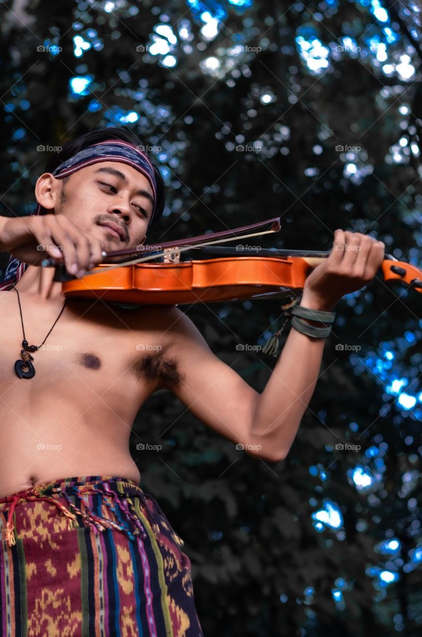 a young man playing violin on the forest