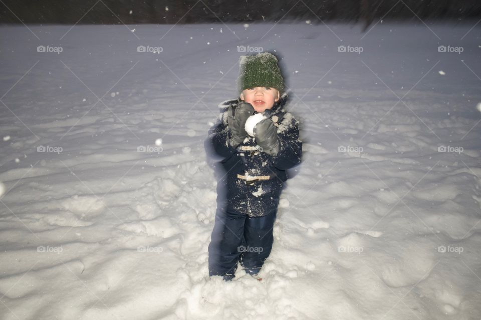 Cute happy 2-year-old toddler boy playing in snow and throwing snow balls during a snow storm 
