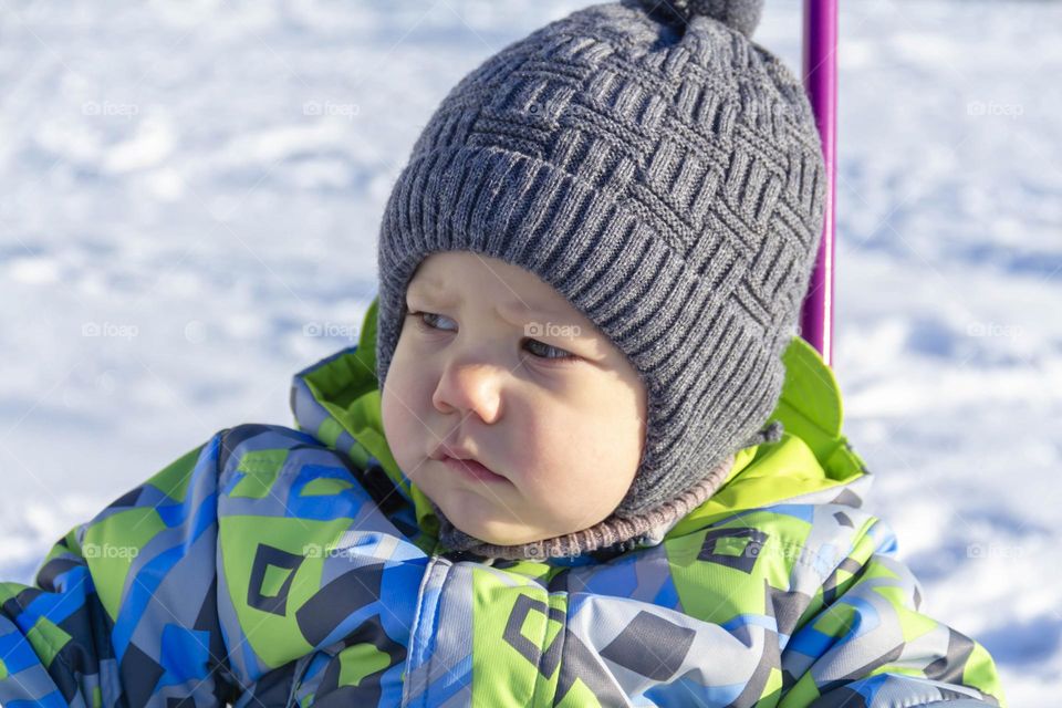 A child in winter in winter jackets, pants, a hat and boots on white snow on the street and in the park in nature plays winter fun and sleds.