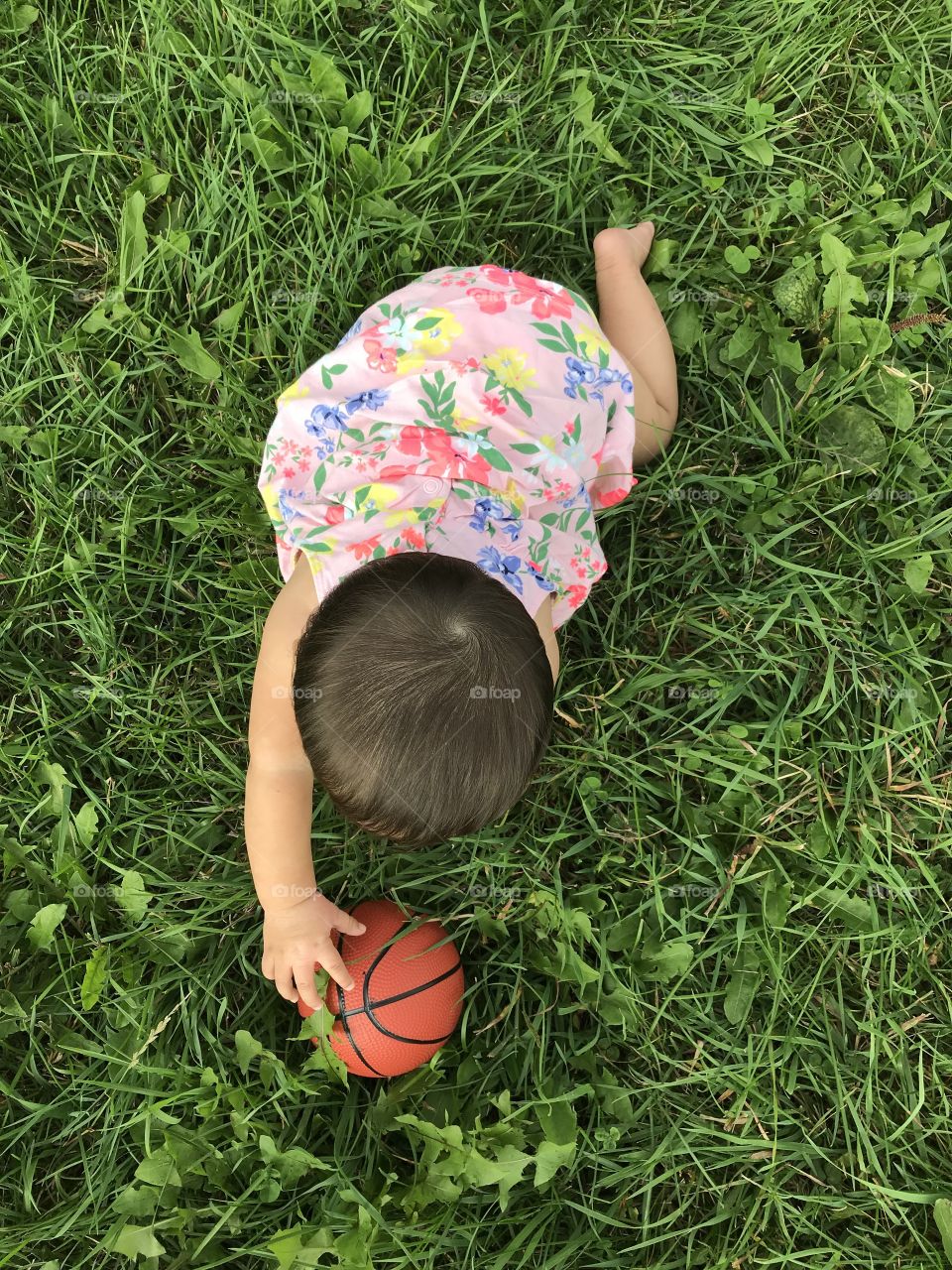 Baby reaching for a toy basketball in grass