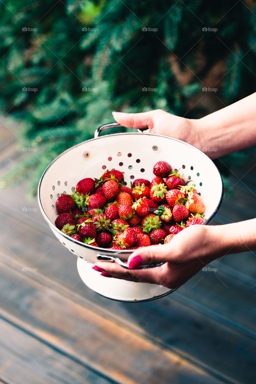 Female hand holding bowl of fresh strawberries sprinkled raindrops over wooden table