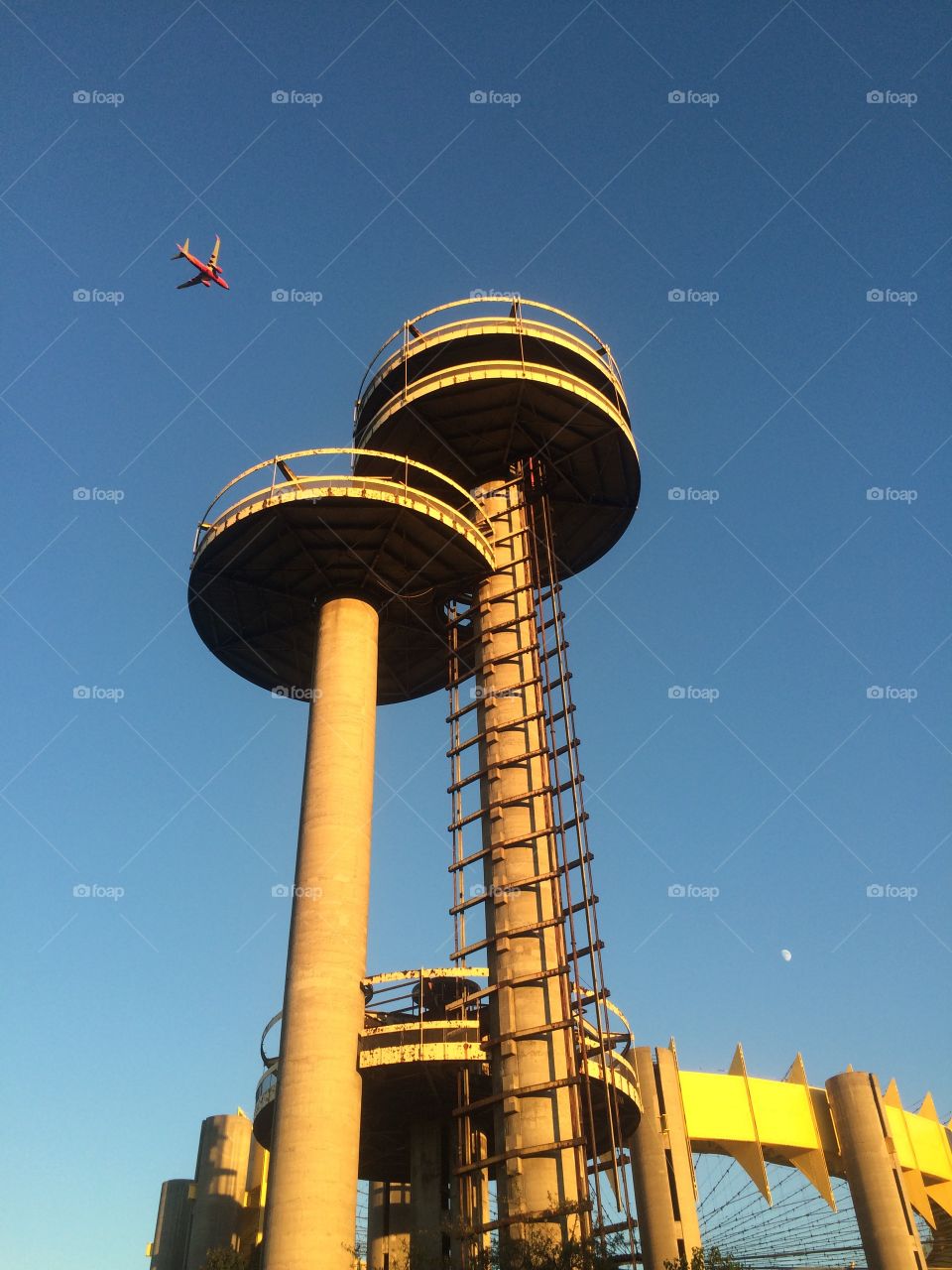 Worlds fair pavilion. Airplane flying over 1964 worlds fair pavilion and observation towers in late day sun
