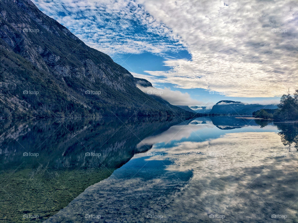 Scenic view of the beautiful reflection of foggy mountains in the green lake in Alps, Slovenia