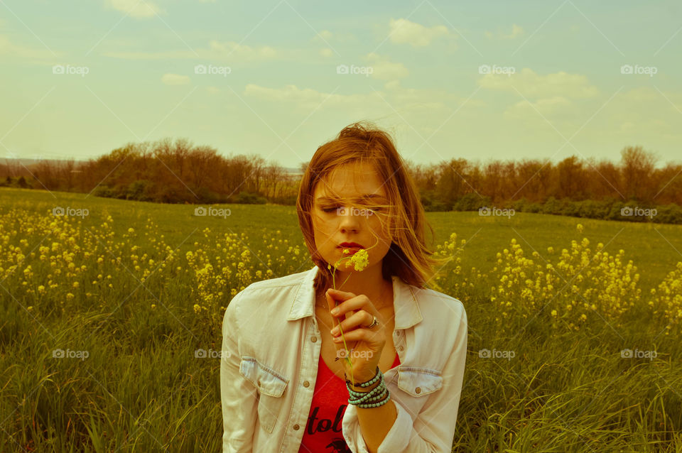 Woman holding and smelling a flower with eyes closed in a field