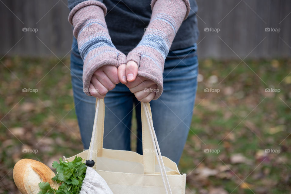 Millennial woman holding reusable grocery bags with fingerless gloves outdoors in the fall